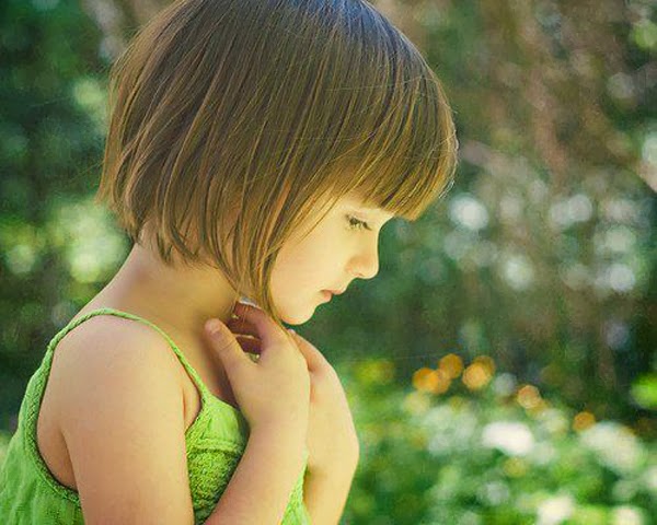 صورة طفلة جميلة بشعر قصير ناعم تضع يديها قرب رقبتها وترتدي الأخضر الفاقع.jpg